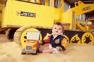 Little boy plays with a digger in the indoor sand pit
